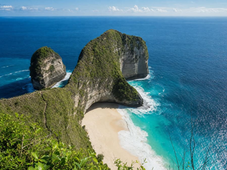 Kelingking Beach on Nusa Penida: a towering green-topped limestone headland dropping in sheer cliffs to a crescent of white sand and turquoise ocean far below.